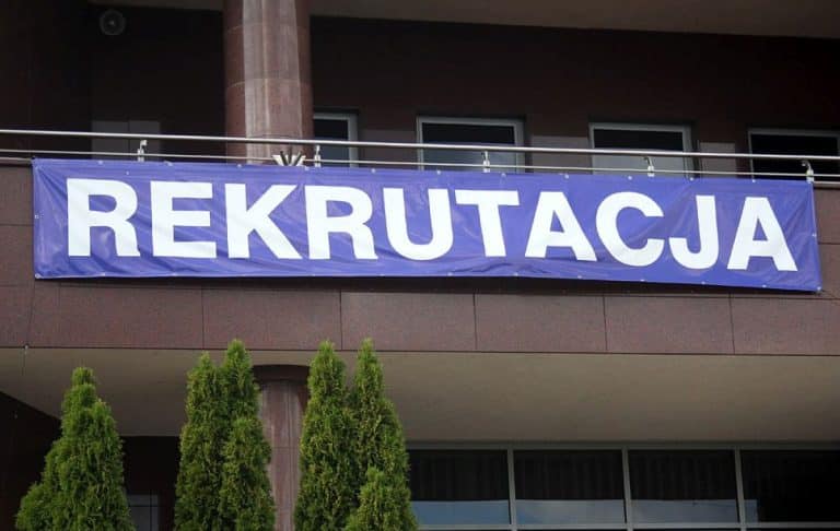 Baner z napisem 'Rekrutacja' na budynku uczelni, nad wejściem do budynku.