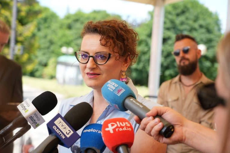 Wiceprezydent Olsztyna udziela wywiadu podczas konferencji, otoczona mikrofonami mediów.