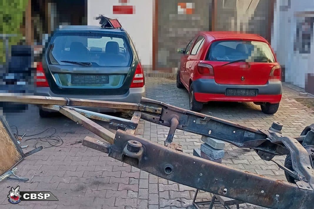 Zdjęcie przedstawia dwa samochody zaparkowane na podwórku, obok znajduje się uszkodzony element pojazdu.
