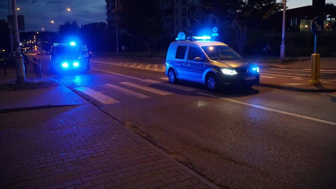 Policja zatrzymuje samochód na ulicy w nocy, na sygnałach świetlnych.