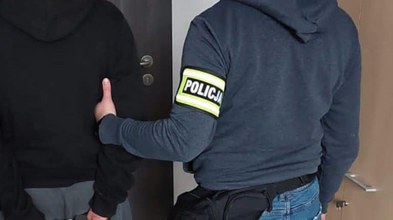 Policjant w mundurze z odznaką 'Policja' zatrzymuje mężczyznę przy drzwiach.