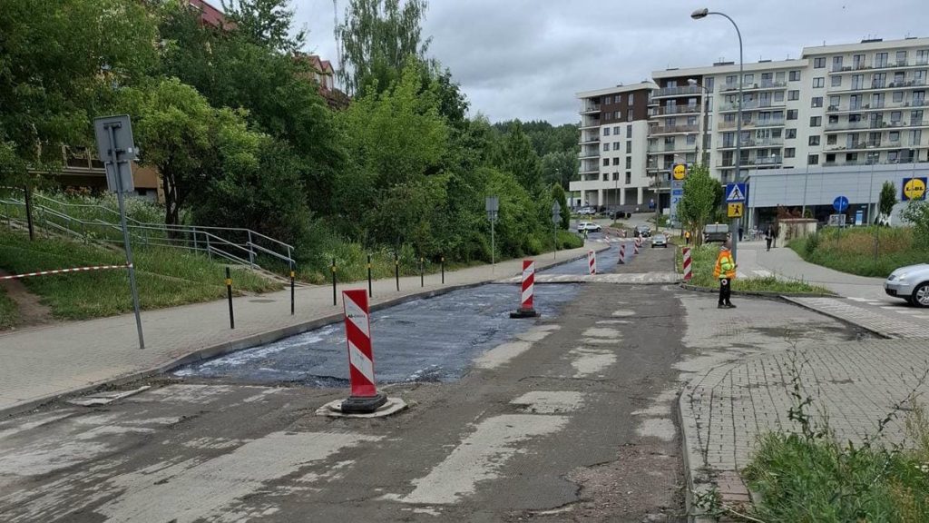 Remontowana ulica z zamkniętym przejazdem, robotnicy i oznakowanie tymczasowe na miejscu.