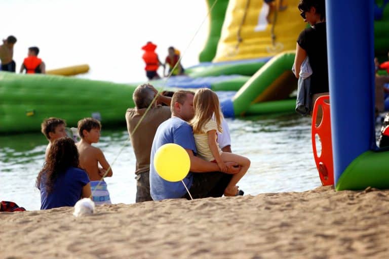 Rodzina siedzi na plaży, w tle duża zjeżdżalnia wodna na jeziorze.
