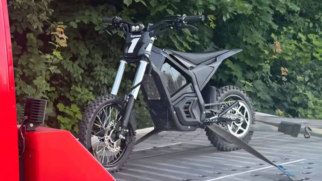 Na zdjęciu odholowany elektryczny motocykl na lawecie, w tle zielone liście i gałęzie.