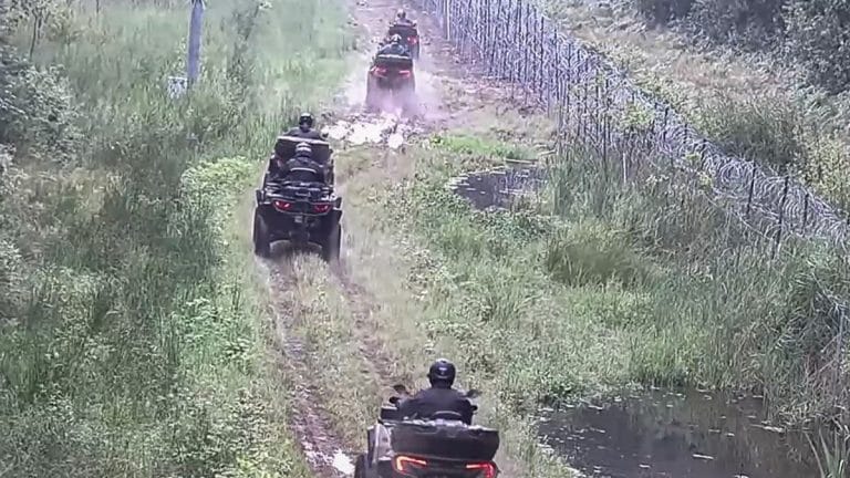 Grupa mężczyzn jadących quadami wzdłuż granicy z Rosją, w terenie z zielenią i drzewami.