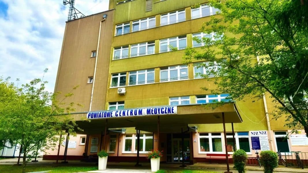 Widok budynku Powiatowego Centrum Medycznego w Braniewie z zielonymi drzewami przed wejściem.