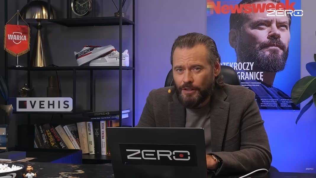Mężczyzna z długim włosem i brodą siedzi przy biurku z laptopem, za nim plakat z mężczyzną i logo Newsweek.