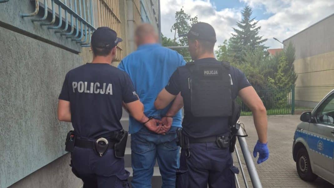 Policjanci zatrzymują mężczyznę przy ścianie, w tle samochód i budynki, na ulicy w Iławie.