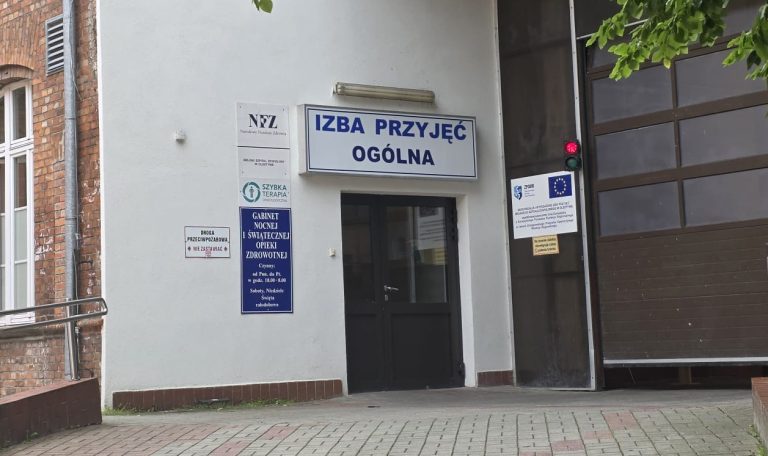Wejście do Izby Przyjęć Ogólnej w szpitalu, z oznaczeniem i informacjami o dostępności nocnej i świątecznej opieki zdrowotnej.