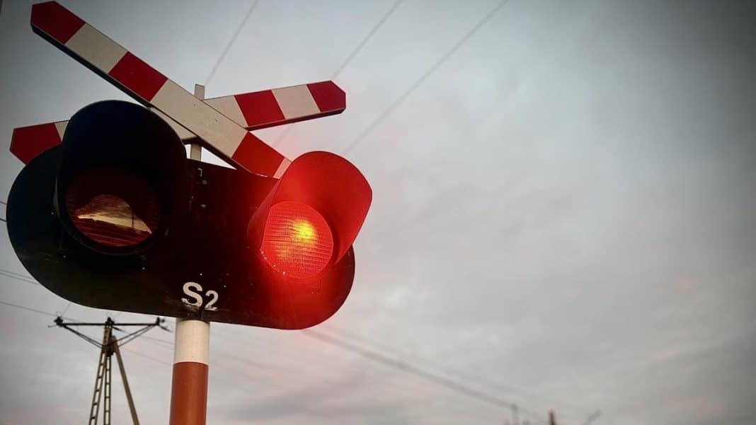 Zdjęcie sygnalizacji świetlnej na przejeździe kolejowym z czerwonym światłem i opuszczonymi rogatkami.
