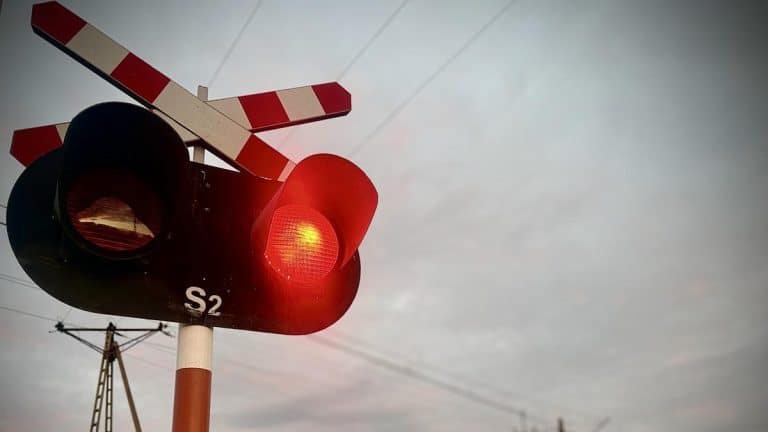 Zdjęcie sygnalizacji świetlnej na przejeździe kolejowym z czerwonym światłem i opuszczonymi rogatkami.