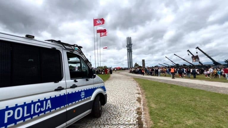 Policja na Polach Grunwaldzkich podczas inscenizacji bitwy, tłumy ludzi i historyczne armaty w tle.