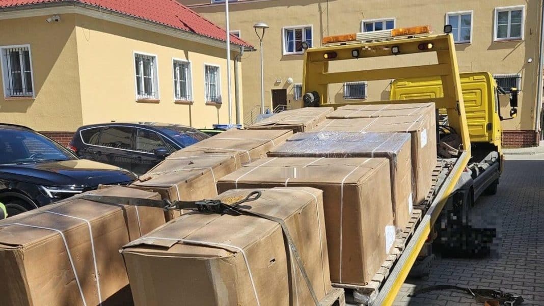 Na zdjęciu widoczny jest żółty samochód z rozładunkiem dużej ilości kartonów na ulicy w pobliżu budynków mieszkalnych.