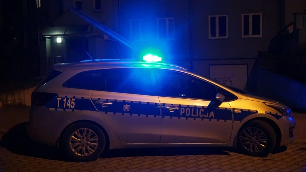 Policja na ulicy w nocy, samochód z włączonymi sygnałami świetlnymi.