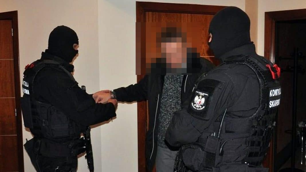 Funkcjonariusze w czarnych mundurach zatrzymują mężczyznę w domu.
