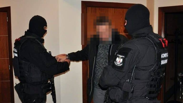 Funkcjonariusze w czarnych mundurach zatrzymują mężczyznę w domu.