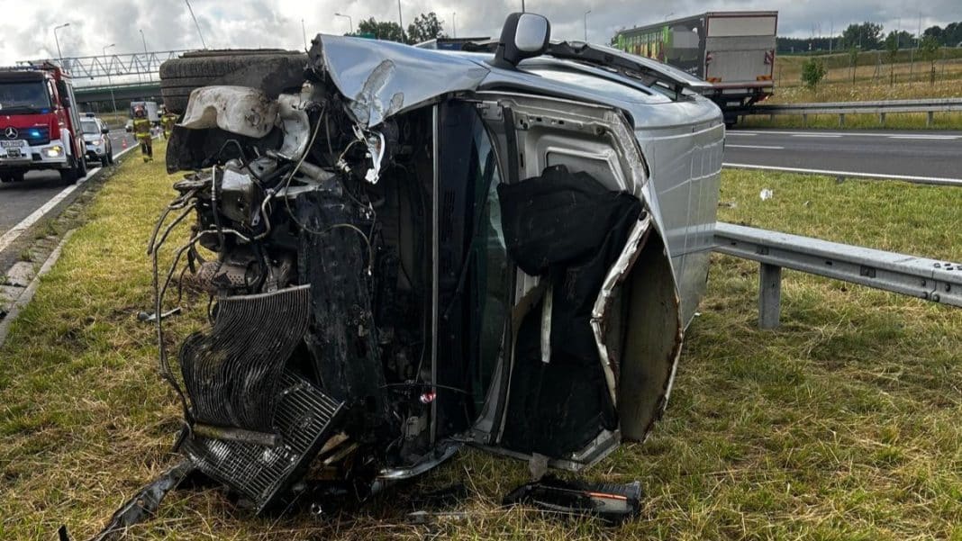 Rozbity samochód na boku na poboczu S7 po wypadku, w tle pojazdy i służby ratunkowe.