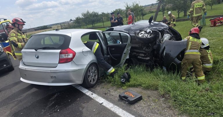 Rozbity samochód na boku w rowie, na miejscu służby ratunkowe i straż pożarna, wypadek na drodze.