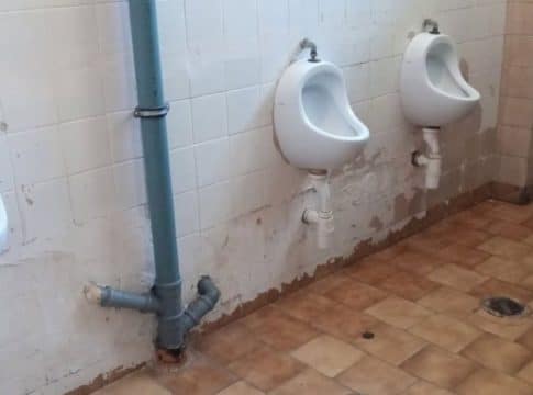 Zdjęcie zniszczonych okien, tynków i placu zabaw na terenie szkoły, widoczne uszkodzenia budynku.