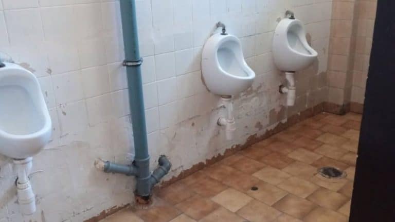 Zdjęcie zniszczonych okien, tynków i placu zabaw na terenie szkoły, widoczne uszkodzenia budynku.
