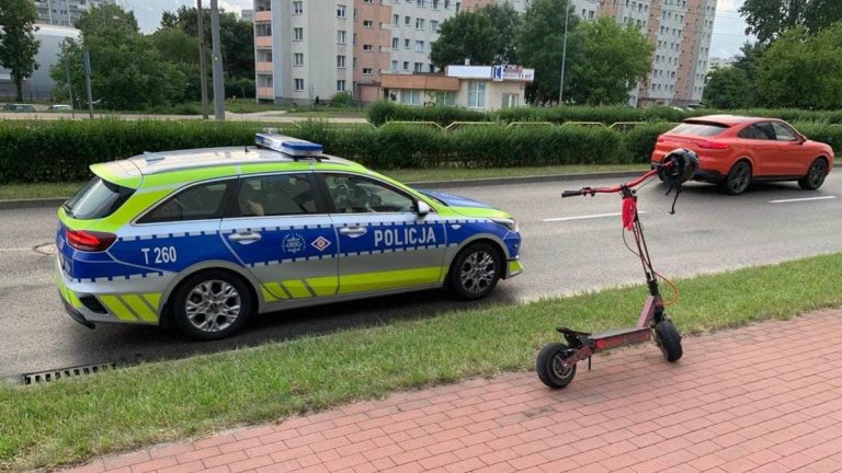 Policja zatrzymuje hulajnogę elektryczną na ulicy w mieście, obok leży kask i hulajnoga.