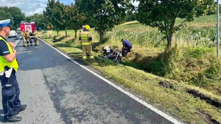 Akcja ratunkowa przy rozbitym motocyklu na drodze krajowej, obecni strażacy i policja.