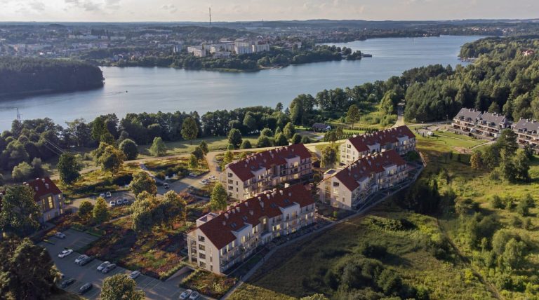 Widok na nowoczesne apartamenty nad jeziorem Czos w Mrągowie, otoczone zielenią i lasami.