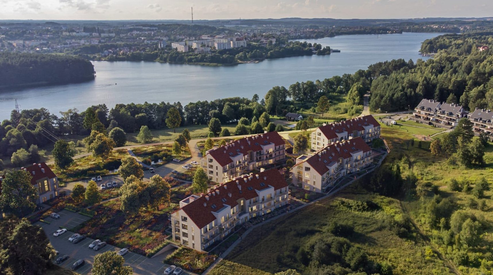 Widok na nowoczesne apartamenty nad jeziorem Czos w Mrągowie, otoczone zielenią i lasami.