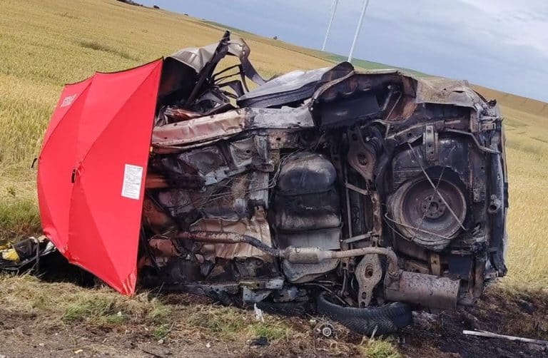 Zniszczony samochód po wypadku na drodze krajowej 16, leżący na polu, z uszkodzonym nadwoziem i rozbitym silnikiem.