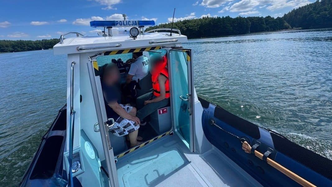 Dwoje mężczyzn na łodzi policyjnej na jeziorze Ukiel, machają rękami, próbując zwrócić na siebie uwagę.