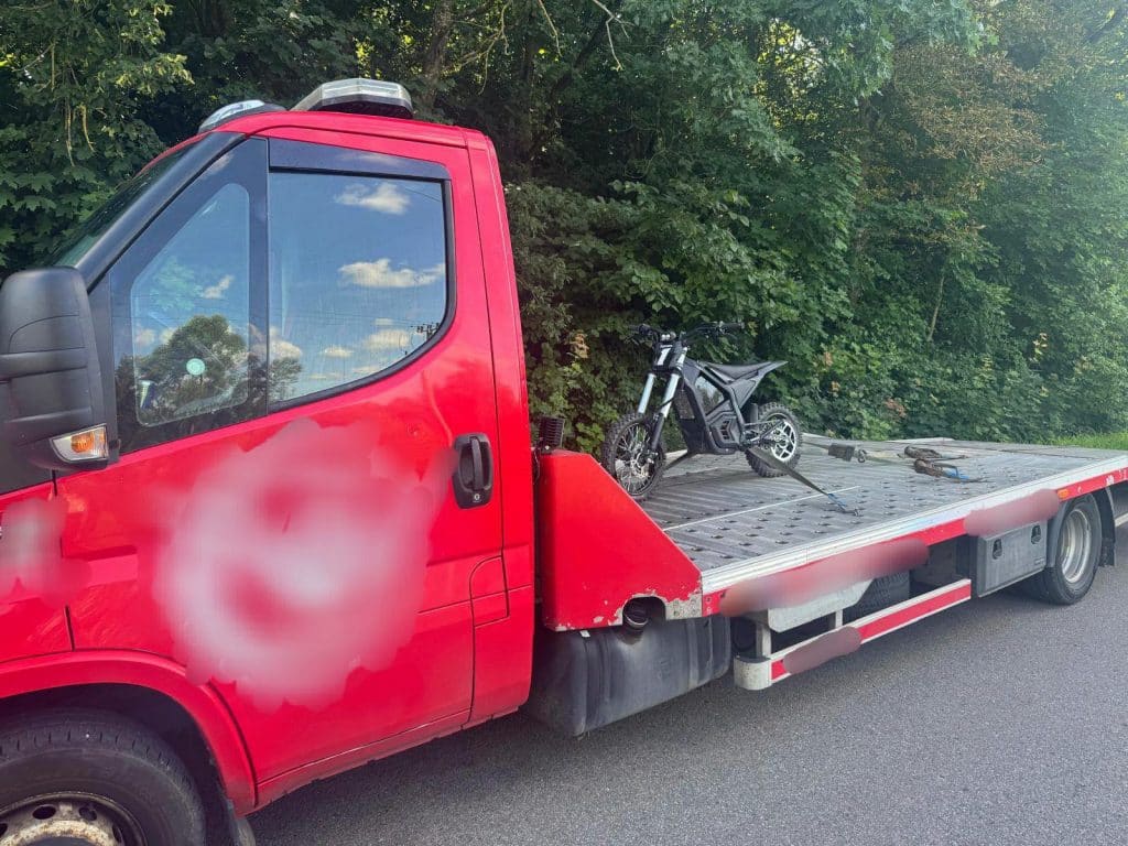 Czerwony samochód laweta z elektrycznym rowerem na platformie, obok zalesiony teren.