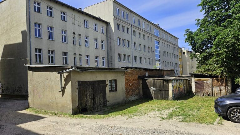 Stare budynki gospodarcze i garaże w centrum Olsztyna, na tle nowoczesnego bloku mieszkalnego.