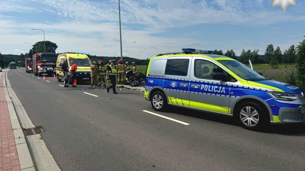 Zdarzenie drogowe na drodze wojewódzkiej z udziałem policji, straży pożarnej i uszkodzonym motocyklem.