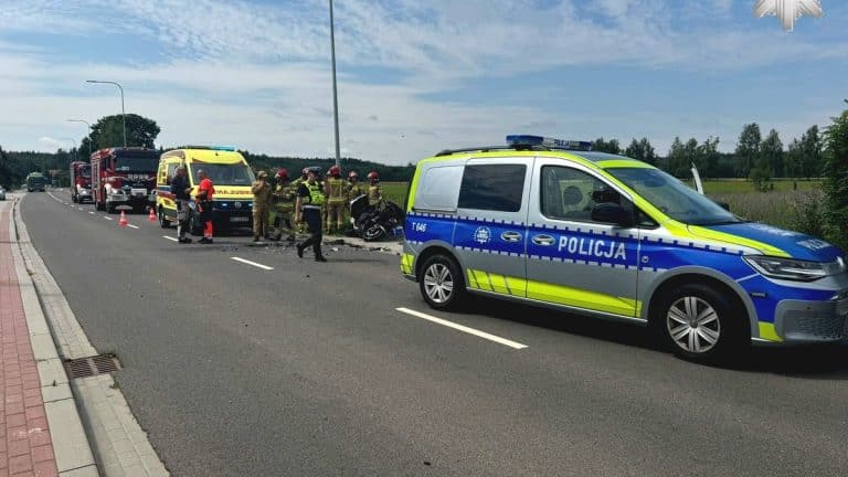 Zdarzenie drogowe na drodze wojewódzkiej z udziałem policji, straży pożarnej i uszkodzonym motocyklem.