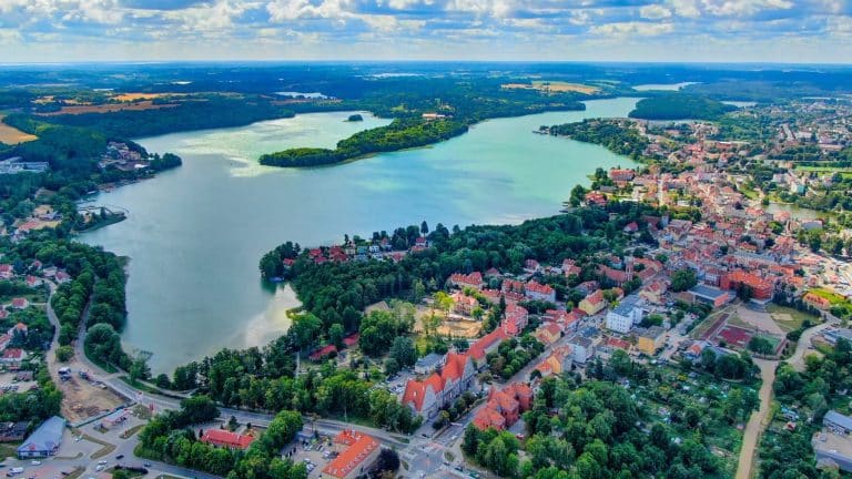 Widok na jezioro Czos i okoliczne tereny z lotu ptaka, zieleń i zabudowania w tle.
