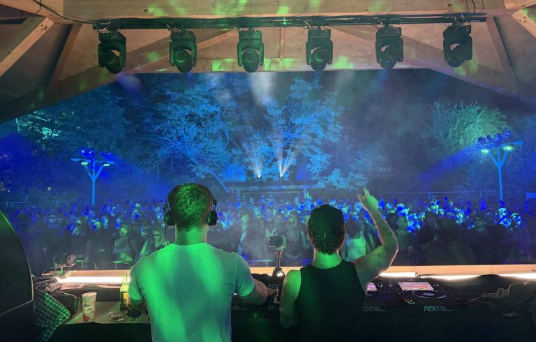 Widok na scenę festiwalową z DJ-ami i tłumem ludzi na Błoniach w Łodzi, oświetlonych kolorowymi światłami.