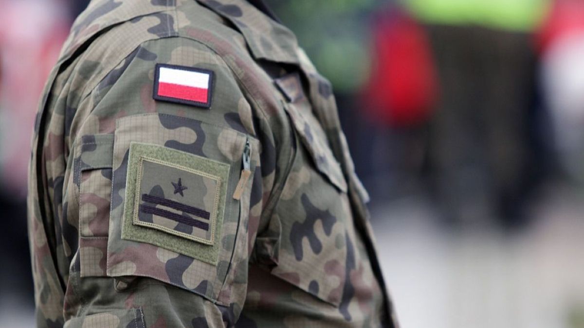 Zdjęcie żołnierza w mundurze wojskowym z polską flagą na ramieniu, z widocznym pagonem i kamuflażem.