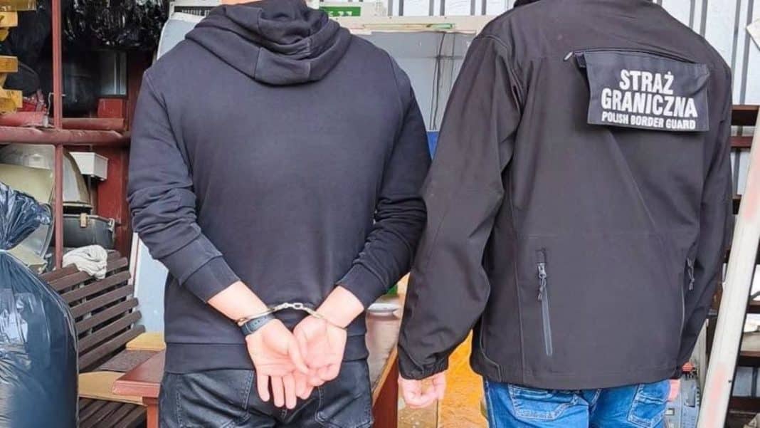 Osoba w rękach zakuta na rękach, obok funkcjonariusz Straży Granicznej w czarnej kurtce z napisem.