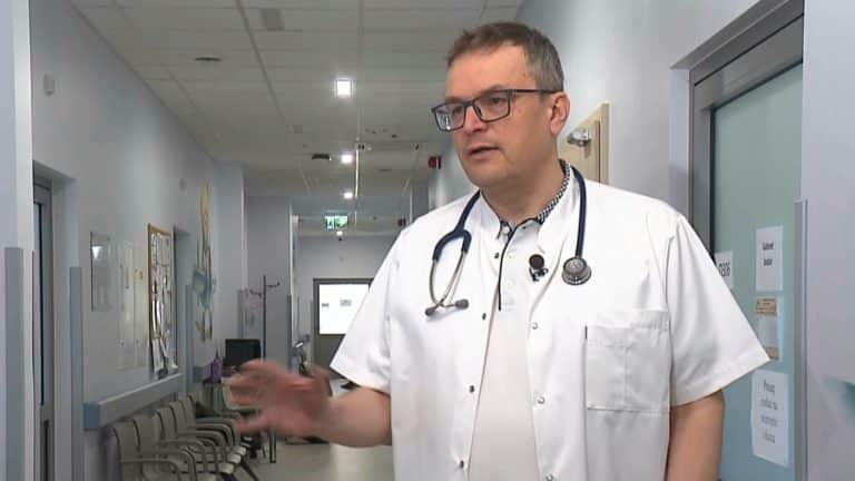 Lekarz w białym kitlu i z stetoskopem rozmawia w szpitalnym korytarzu.