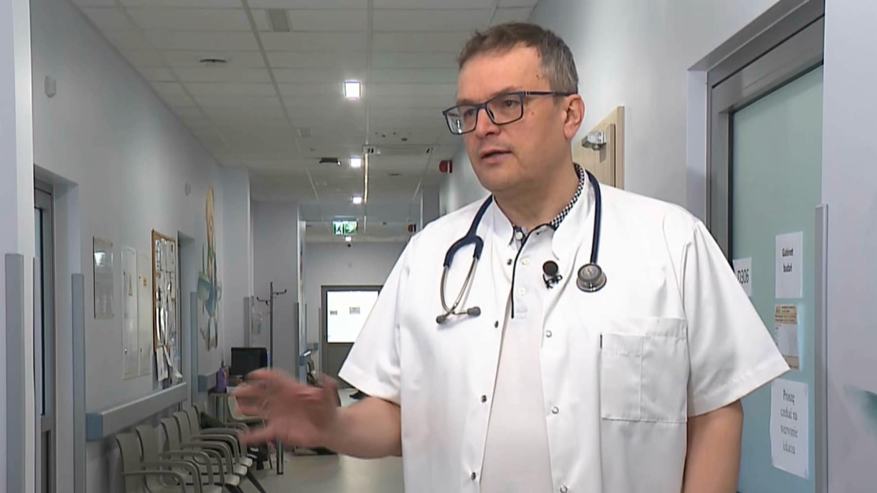 Lekarz w białym kitlu i z stetoskopem rozmawia w szpitalnym korytarzu.