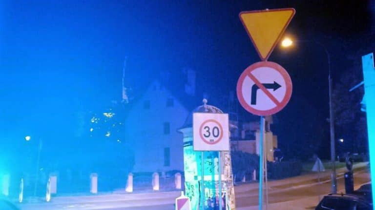 Zdjęcie nocne z ulicy, na którym widać znaki drogowe i oświetlenie, bez ludzi na pierwszym planie.