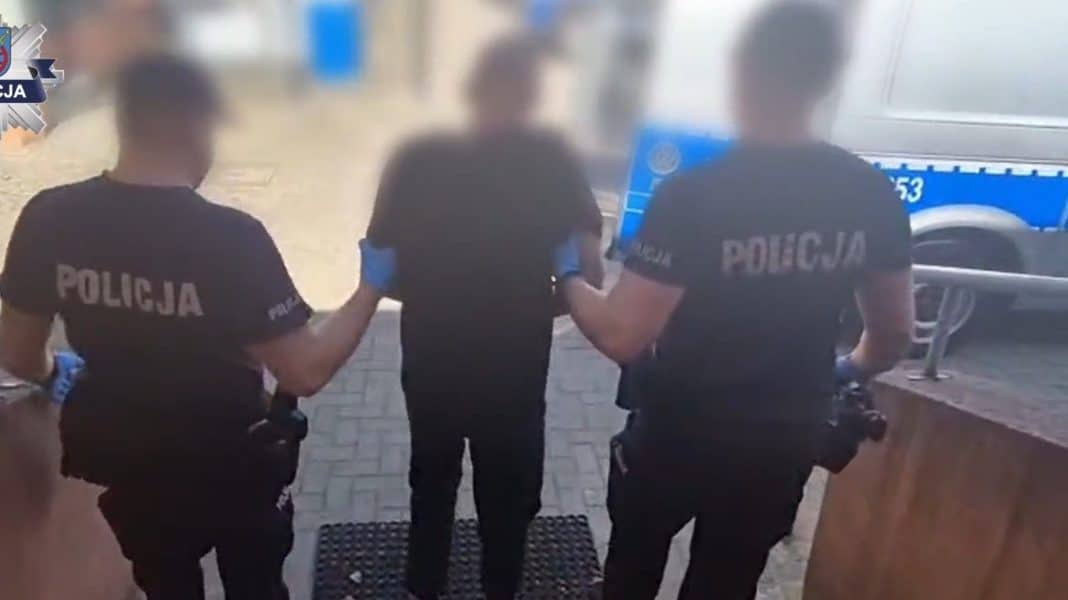 Trzech policjantów prowadzi mężczyznę w rękach, w tle radiowóz policyjny.