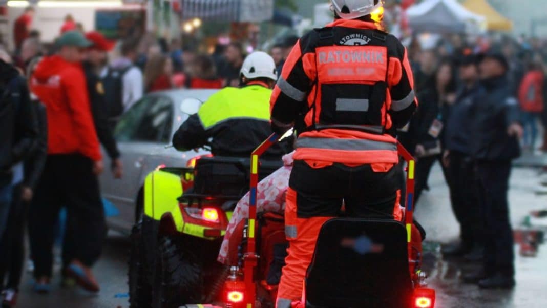 Ratownicy medyczni na motorze podczas akcji ratunkowej na ulicy w tłumie ludzi.