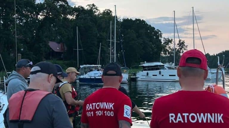 Grupa ratowników i strażaków na łodzi nad jeziorem Kisajno podczas akcji poszukiwawczej.