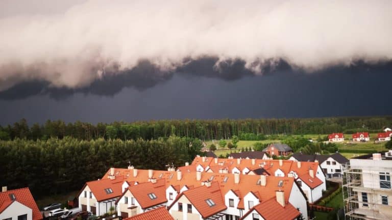 Ciemne, burzowe chmury nad zabudową mieszkaniową na tle lasu na Warmii i Mazurach.