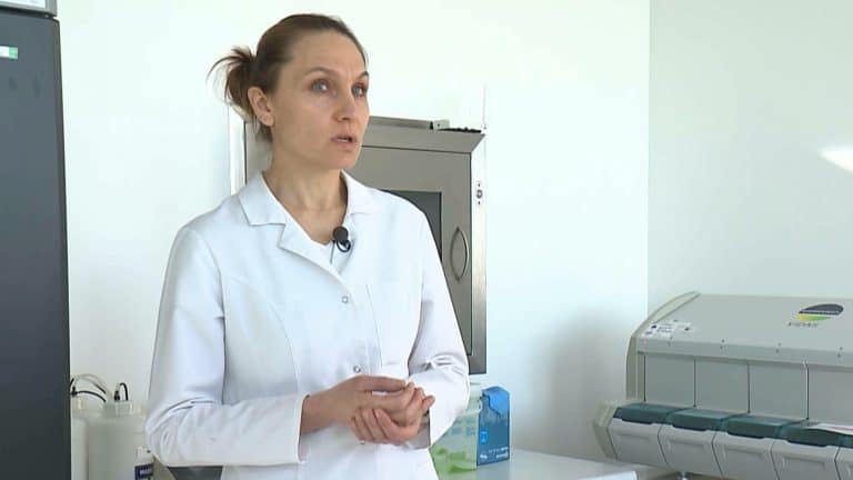 Lekarka w białym kitlu opowiada o zagrożeniach związanych z kleszczami, w tle urządzenia medyczne.