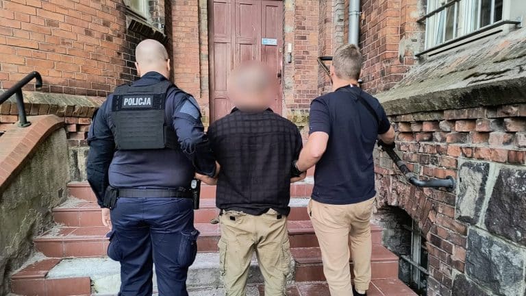 Trzech policjantów zatrzymuje poszukiwanego mężczyznę na schodach przy kamienicy na starówce.