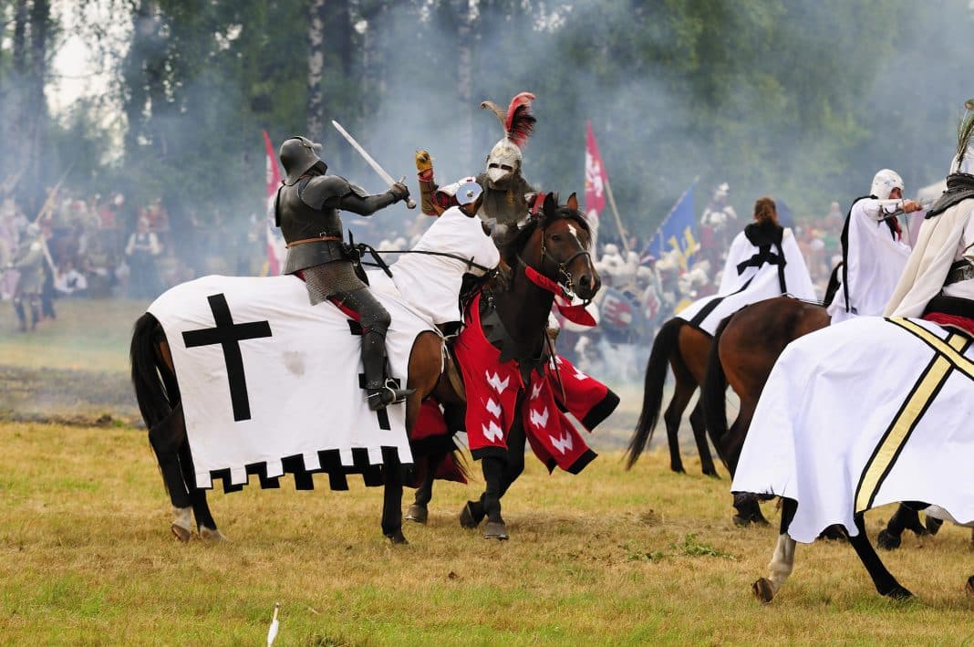 Rekonstrukcja bitwy na polu z rycerzami na koniach w średniowiecznych strojach i z tarczami.
