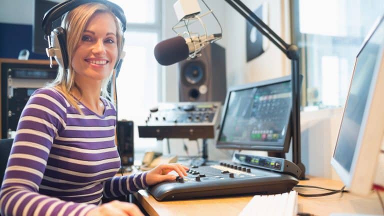 Kobieta w słuchawkach przy mikrofonie i komputerze w studiu radiowym.
