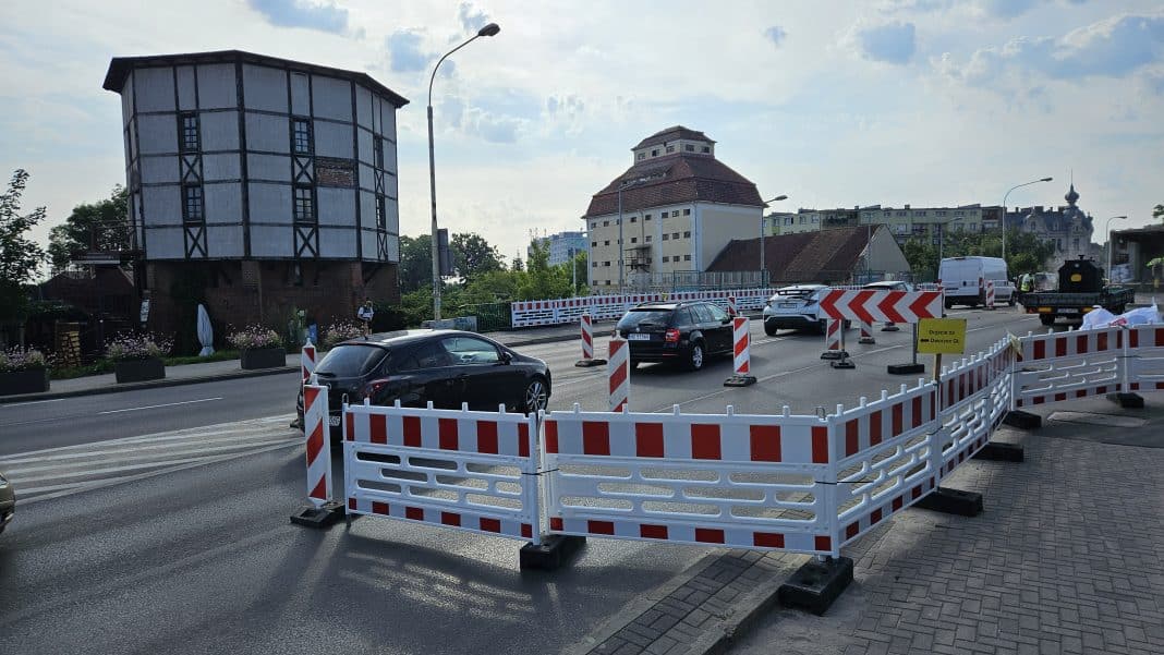 Ulica Limanowskiego w Olsztynie z zamkniętym pasem ruchu i barierami, w tle widoczny wiadukt i budynki.